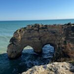 A natural double rock arch in the golden cliffs of the Algarve coast in Portugal, waves washing through it