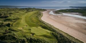 A links green beside a wide sandy shore in Ireland