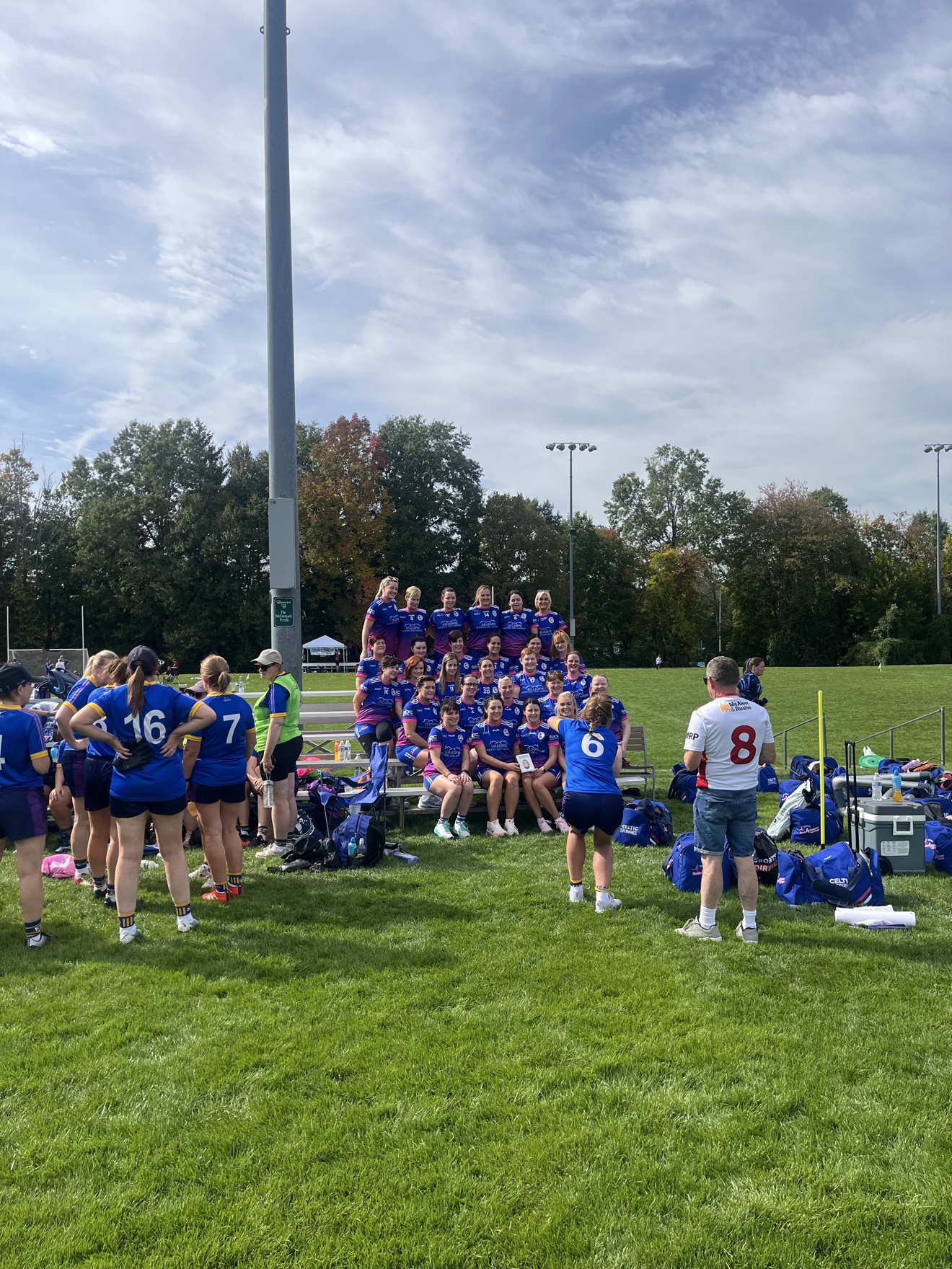 Ladies GAA Mothers & Others tournament at Rockland GAA — team photo on the pitch, players in blue and purple on the bleachers