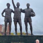 JP Cone in front of the United Trinity statue of George Best, Denis Law and Bobby Charlton at Old Trafford