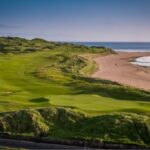 A links green with dunes and a sandy bay behind it in Ireland