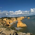 Golden limestone cliffs and sea stacks along the Algarve coast in Portugal under a blue sky