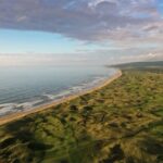 A Scottish links golf course stretching along a golden beach under a wide sky
