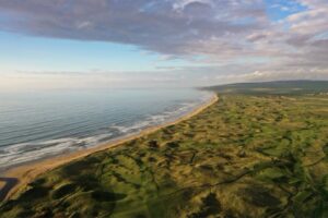 A Scottish links golf course stretching along a golden beach under a wide sky
