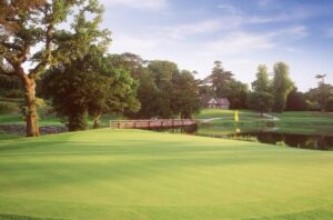 A parkland golf course in Ireland with a lake, bridge and country house