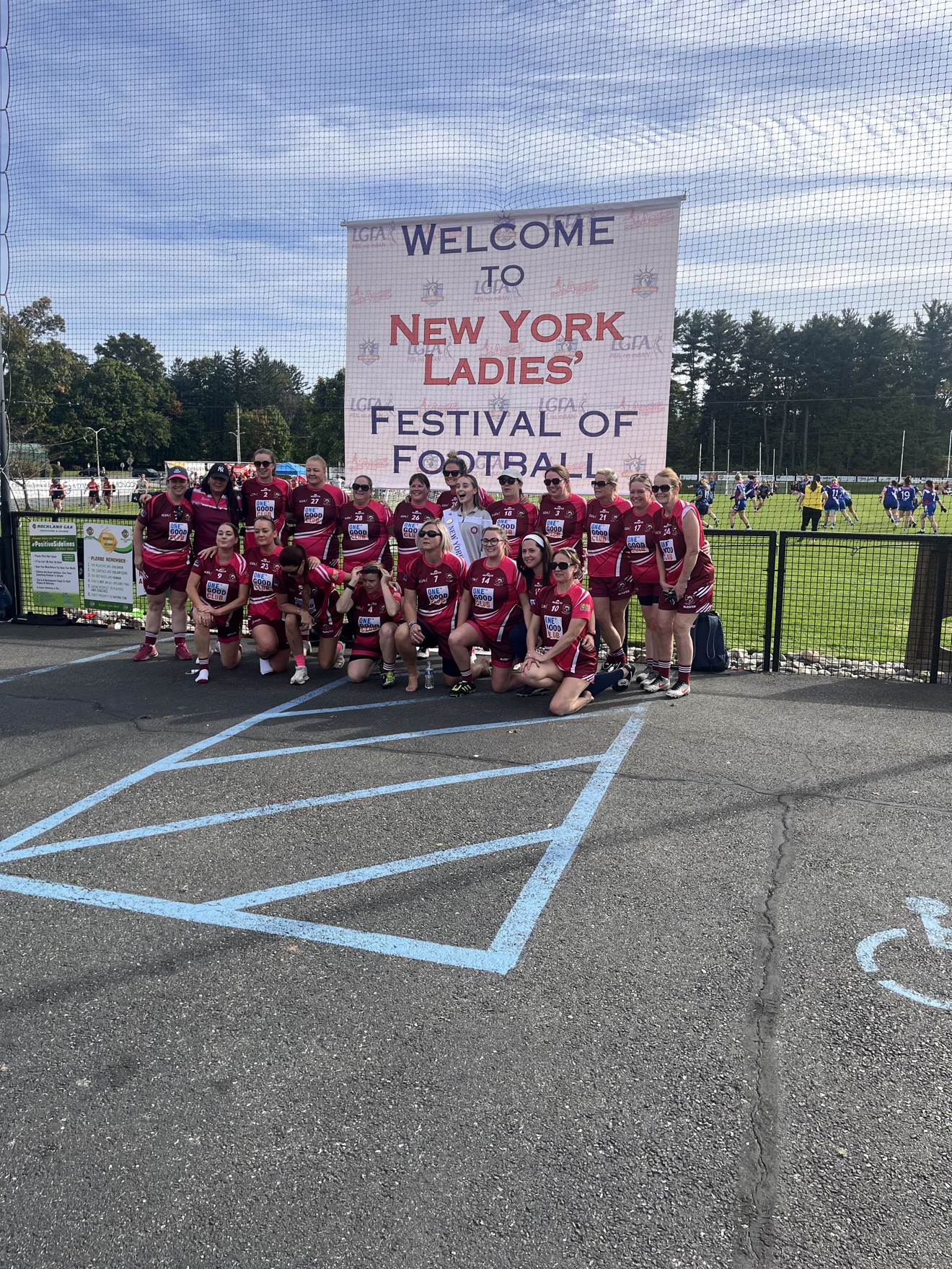 Saint Raymond's GAA ladies volunteering — team in maroon in front of the Welcome to New York Ladies' Festival of Football banner