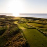 An aerial view of an English links at sunset with the Irish Sea beyond