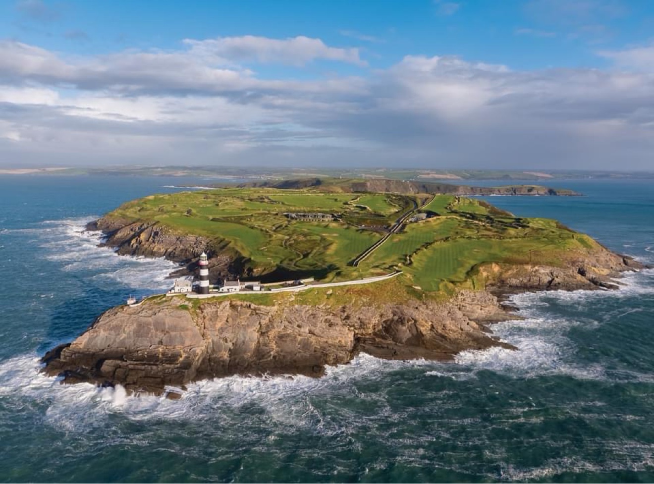 Aerial view of Old Head Golf Links on its headland with the black-and-white lighthouse
