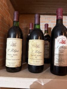 Dusty vintage bottles of S. Filipe red wine from Terras do Sado in Portugal — the 1995, 1997 and 2000 vintages — resting in a cellar