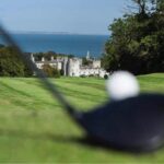 A tee shot on an Irish coastal course, a castle by the sea beyond