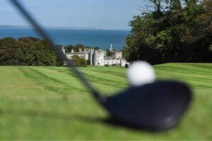 A tee shot on an Irish coastal course, a castle by the sea beyond
