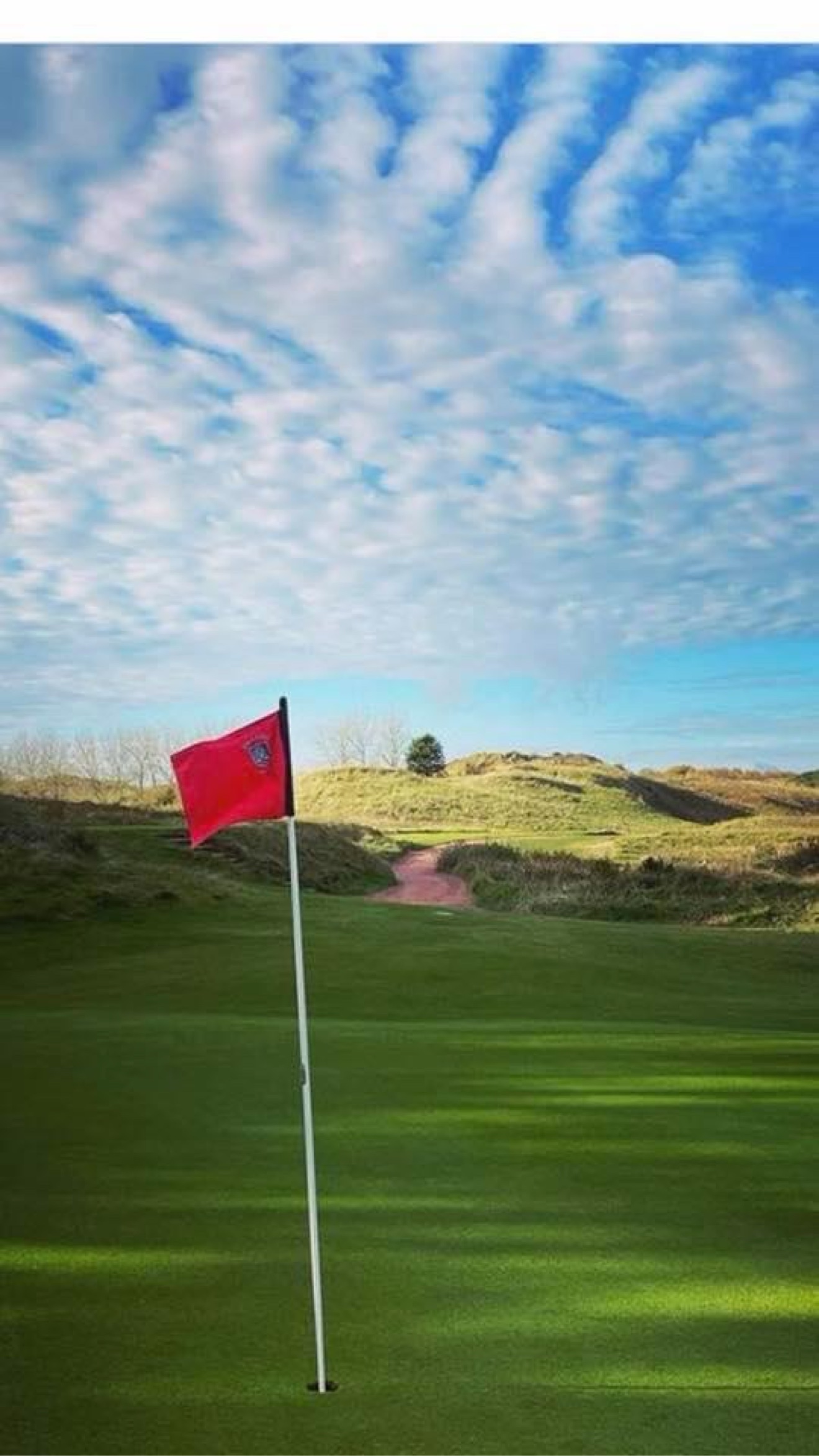 Red flagstick on a links green with dunes behind