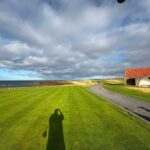 A coastal links tee in Scotland beside a small stone shelter with a red-tiled roof, the sea beyond