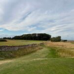 A Scottish links fairway running beside an old stone wall, with the sea in the distance