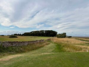 A Scottish links fairway running beside an old stone wall, with the sea in the distance