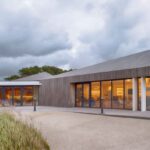 A modern timber clubhouse glowing at dusk on England's Golf Coast