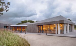 A modern timber clubhouse glowing at dusk on England's Golf Coast