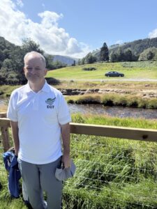 JP of EGT in his EGT polo at Glendalough, the river and the round tower behind him