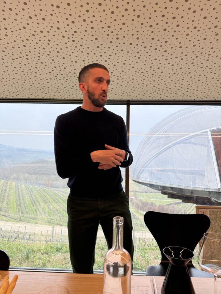 A host presents a wine tasting at the Ceretto winery in Piedmont, Italy, the estate's vineyards and famous glass dome behind him