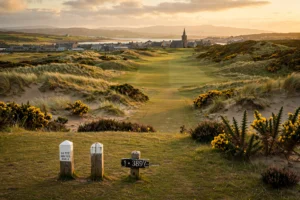 The first tee of a Highland links golf course with a town and church spire behind
