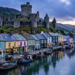 A medieval castle above a harbour town in Wales at dusk, colourful houses along the quay